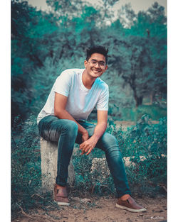 Portrait of smiling young man sitting against trees