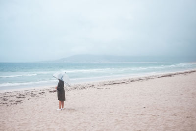 Rear view of woman on beach against sky