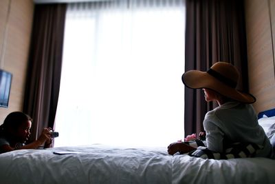 Girl photographing mother relaxing on bed at home