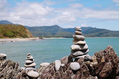 Stack of stones on rocks by sea against sky