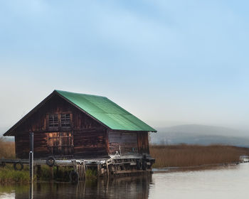 House by lake against sky