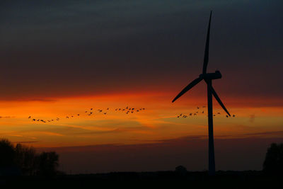Silhouette windmills against sky during sunset