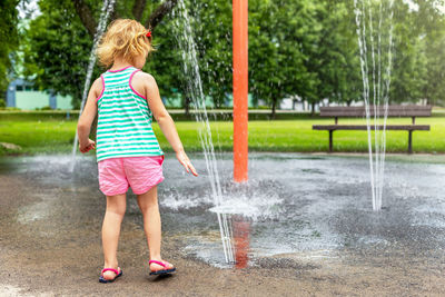 Little smiling child playing with water at splash pad in the local public park on hot summer day. 