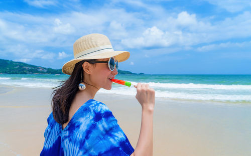 Woman eating popsicle at beach against sky
