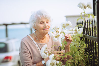 Elderly woman admiring beautiful bushes with white roses