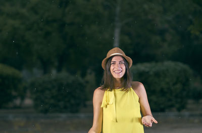 Portrait of smiling woman wearing hat standing against trees on road