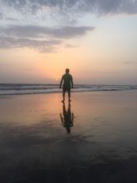 Rear view of silhouette man standing at beach during sunset