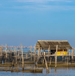 Wooden posts on house by sea against clear sky