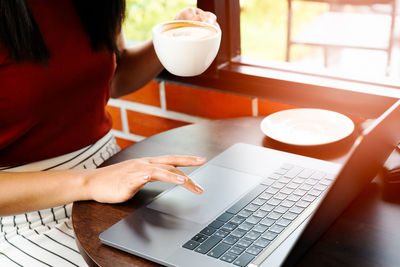 Asia woman hold cup of coffee while typing on laptop keyboard. w