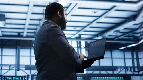 Side view of businessman using laptop while standing in city