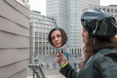 Portrait of woman holding mirror in city
