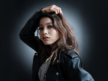 Portrait of young woman standing against black background