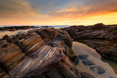 Rock formation on beach against sky during sunset