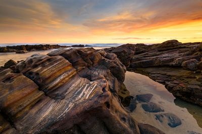 Rock formation on beach against sky during sunset