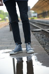 Low section of person standing by puddle at railroad station platform