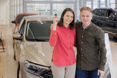 Portrait of young woman standing against car