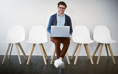 Smiling man using laptop sitting on chair