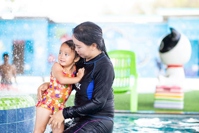 Mother embracing daughter while sitting in water park