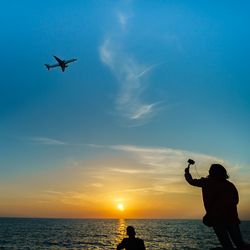 Low angle view of silhouette man photographing airplane against sky during sunset
