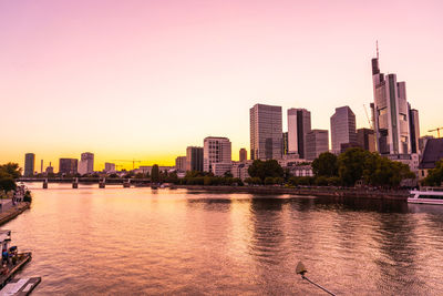 River by buildings against sky during sunset