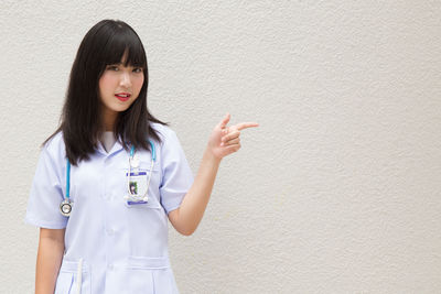 Young female doctor standing against wall