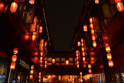 Low angle view of illuminated lanterns hanging amidst buildings at night