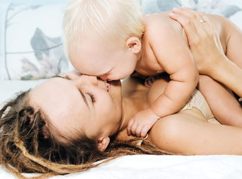 Mother playing with naked daughter on bed at home