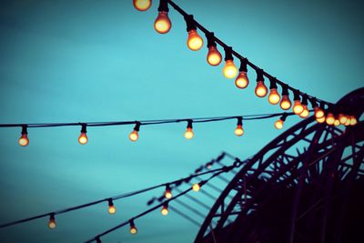 Low angle view of illuminated light bulbs hanging against sky