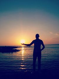 Optical illusion of man holding sun while standing at beach during sunset