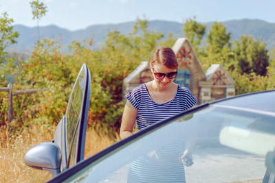 Woman in sunglasses standing by car during sunny day