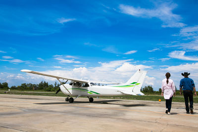 Rear view of people walking at airport runway against sky