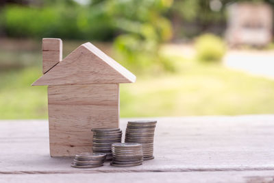 Close-up of wooden model home with coins on wooden table against plants