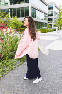 Happy young woman in pink shirt turning around with backpack on street