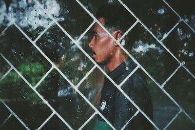 Side view of man looking away seen through wet glass window during rainy season