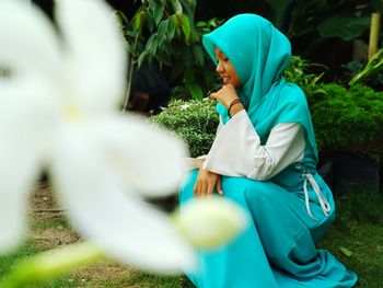 Young woman wearing hijab crouching by plants at park