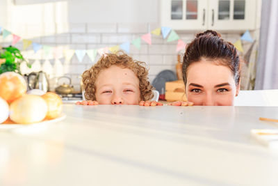 Portrait of playful mother and son hiding behind kitchen island