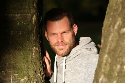 Portrait of smiling young man against tree trunk