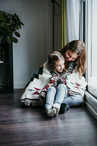 Girl sitting on sitter lap while sitting by window at home