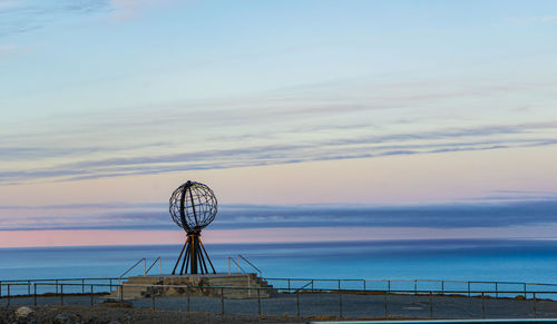 Ferris wheel by sea against sky at sunset