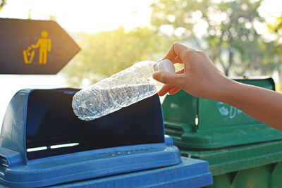 Close-up of hand throwing bottle into trash can