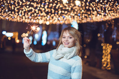 Portrait of smiling woman holding illuminated sparkler at night