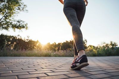 Low section of woman walking on footpath against sky