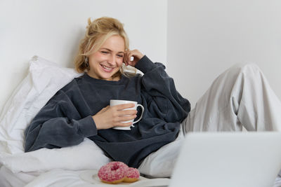Portrait of young woman using laptop while sitting on bed at home