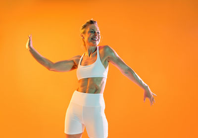 Full length of woman with arms raised standing against yellow background