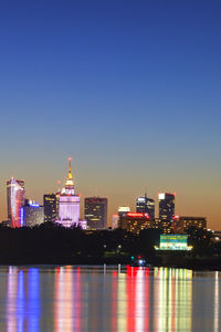 Illuminated buildings in city against clear sky at night