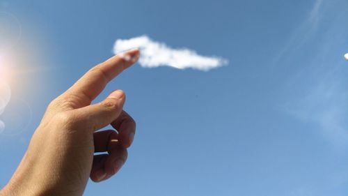 Cropped hand of person pointing at clouds in sky