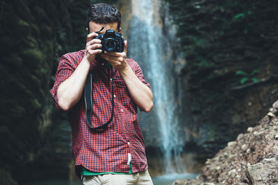 Man photographing through digital camera against waterfall