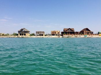 Buildings by sea against clear sky