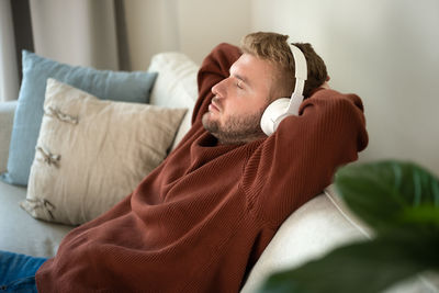 Young caucasian blond curly hair man listening to music with big white handsfree headphones 