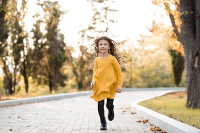 Pretty funny kid girl 5-6 year oldwear yellow stylish dress run in autumn park outdoor.
